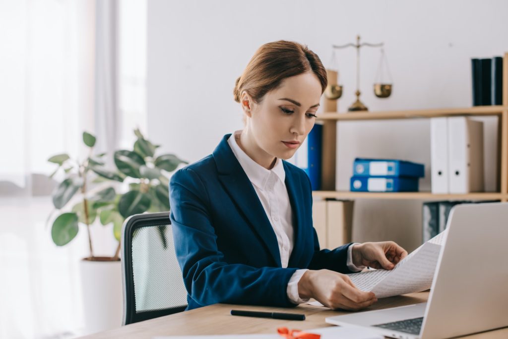 side view of concentrated female lawyer working with documents at workplace in office